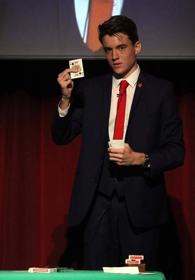 George Berryman performing magic on stage under a spotlight.